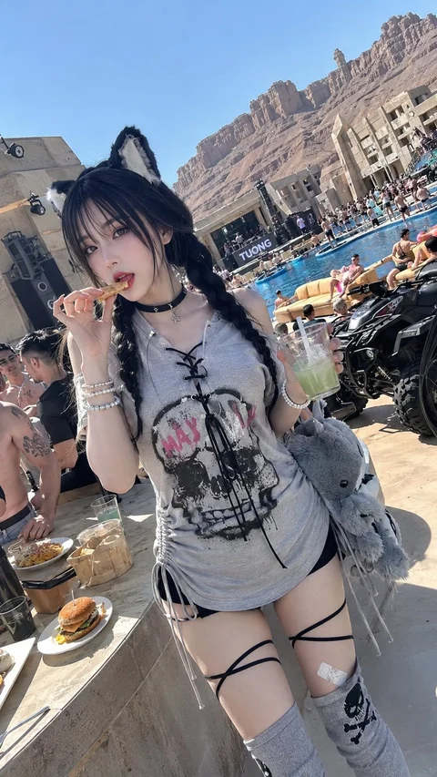 A woman wearing a cat-ear headband, graphic shirt and gray socks stands at a sunny poolside gathering.